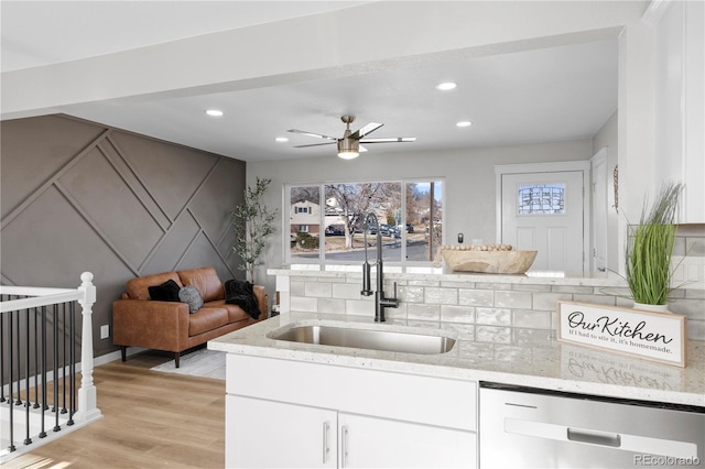 kitchen with dishwasher, sink, light wood-type flooring, light stone counters, and white cabinetry