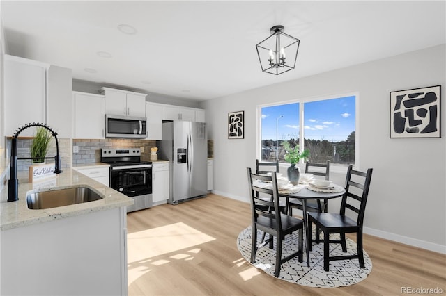 kitchen featuring stainless steel appliances, a sink, light wood finished floors, and decorative backsplash