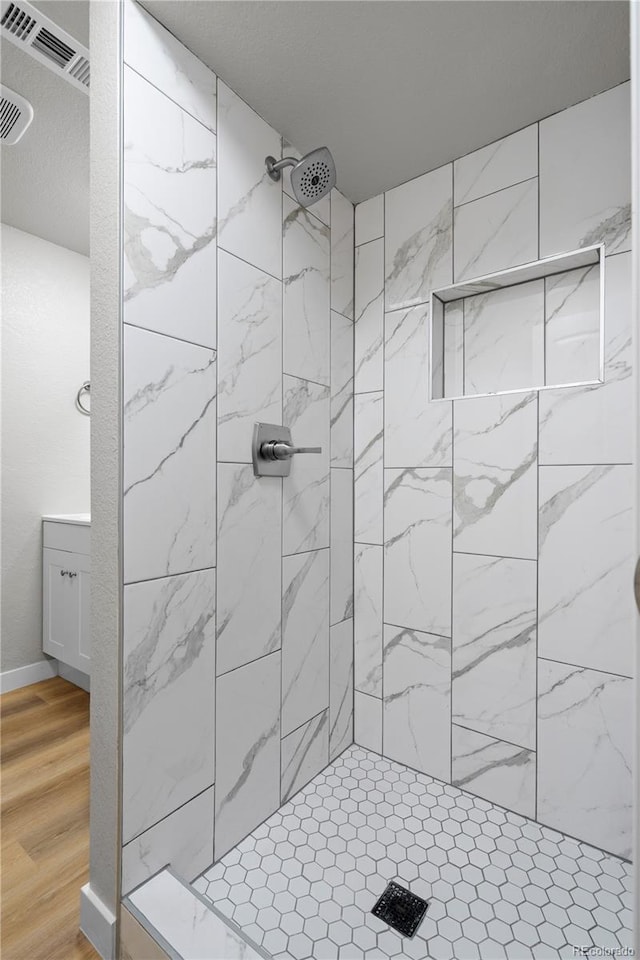 full bath with visible vents, a tile shower, and wood finished floors