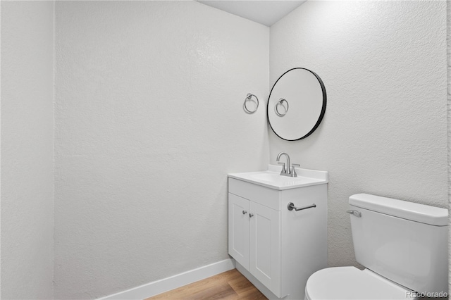 bathroom featuring a textured wall, toilet, wood finished floors, vanity, and baseboards