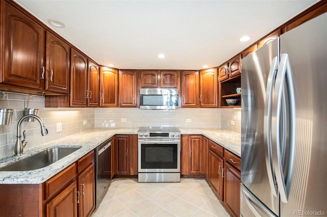 kitchen with light tile patterned floors, a sink, appliances with stainless steel finishes, backsplash, and light stone countertops