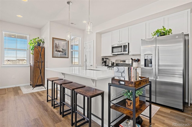 kitchen featuring white cabinetry, decorative light fixtures, appliances with stainless steel finishes, a wealth of natural light, and a kitchen island with sink