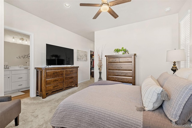 carpeted bedroom with ensuite bath, a walk in closet, and ceiling fan