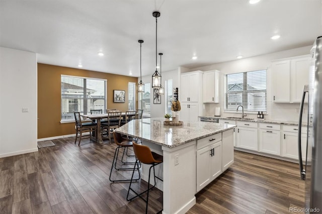 kitchen featuring a breakfast bar area, dark wood-type flooring, a kitchen island, white cabinetry, and freestanding refrigerator