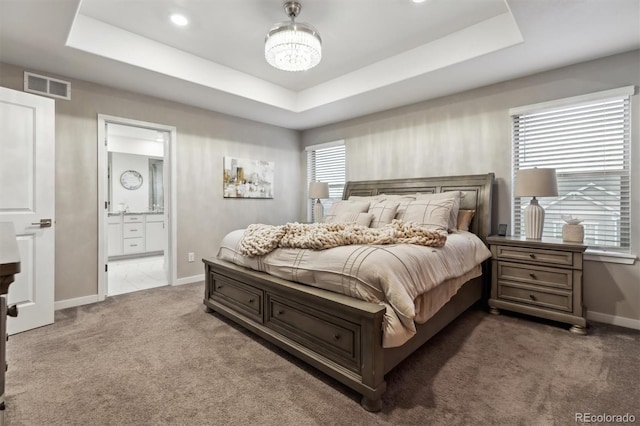 carpeted bedroom with a chandelier, connected bathroom, visible vents, baseboards, and a tray ceiling