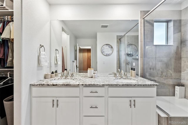 full bath featuring double vanity, a stall shower, a walk in closet, and a sink