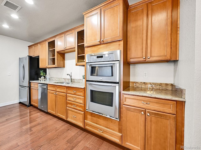 kitchen featuring visible vents, light stone countertops, light wood-style flooring, stainless steel appliances, and a sink