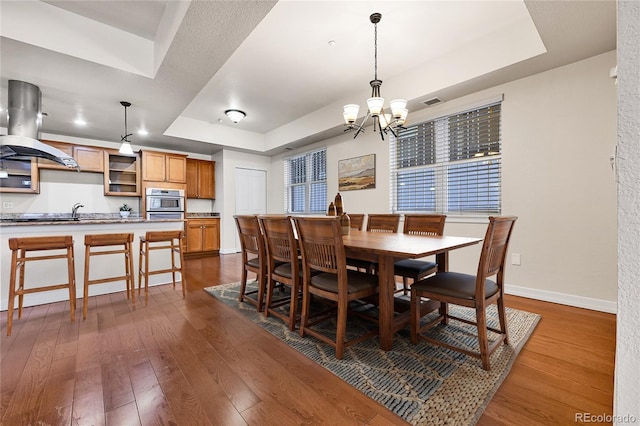 dining space with dark wood-style floors, a chandelier, baseboards, and a tray ceiling