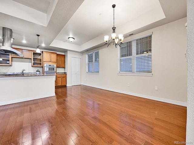 kitchen featuring a raised ceiling, an inviting chandelier, island range hood, baseboards, and dark wood-style flooring