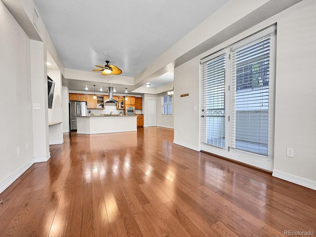 unfurnished living room with dark wood finished floors, baseboards, ceiling fan, and a sink