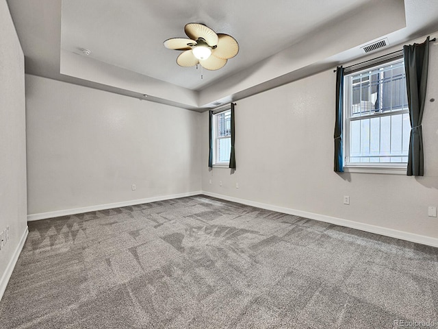 unfurnished room with a tray ceiling, carpet, visible vents, and baseboards