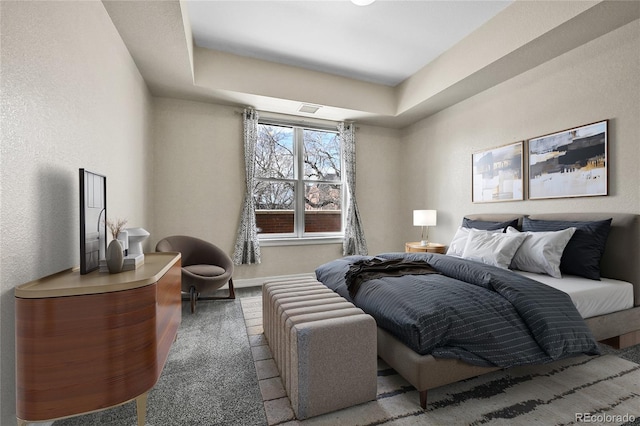 carpeted bedroom with visible vents, a raised ceiling, baseboards, and a textured wall