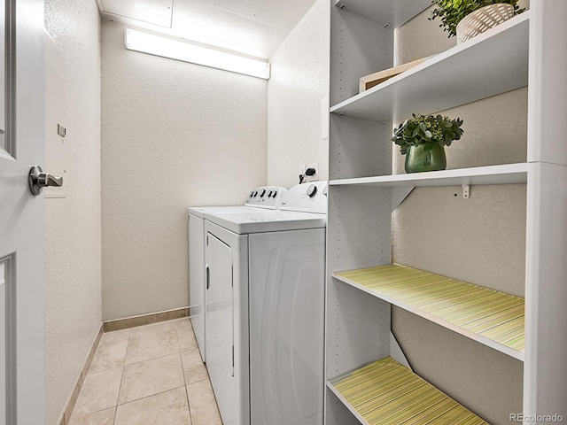 clothes washing area featuring washer and dryer, light tile patterned flooring, baseboards, laundry area, and a textured wall