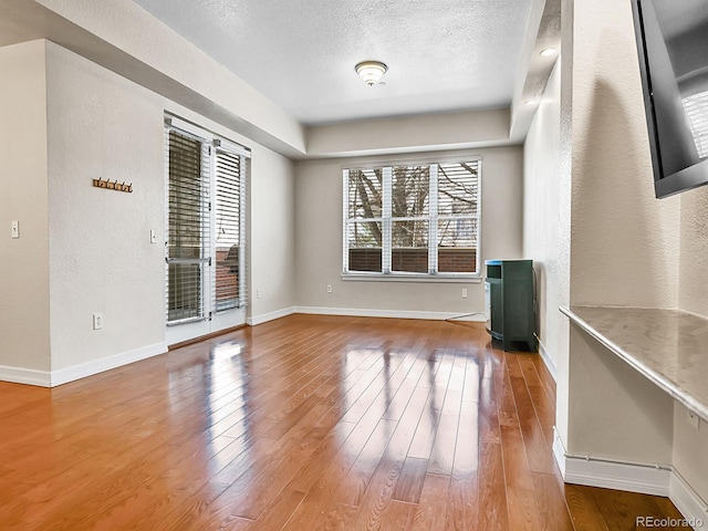 interior space with a textured wall, a textured ceiling, baseboards, and hardwood / wood-style flooring