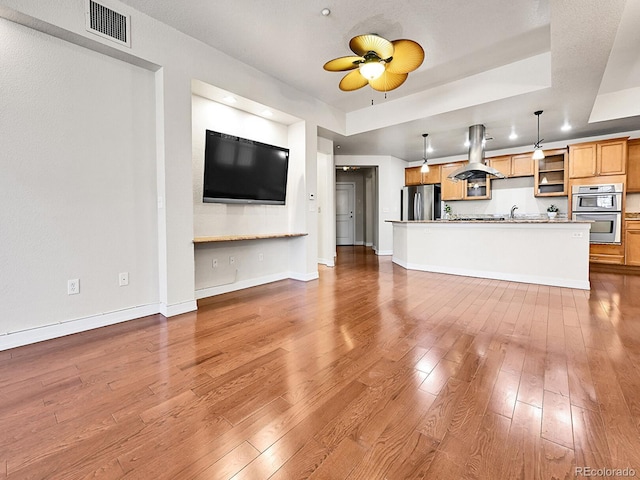 unfurnished living room featuring a tray ceiling, hardwood / wood-style flooring, visible vents, and a sink