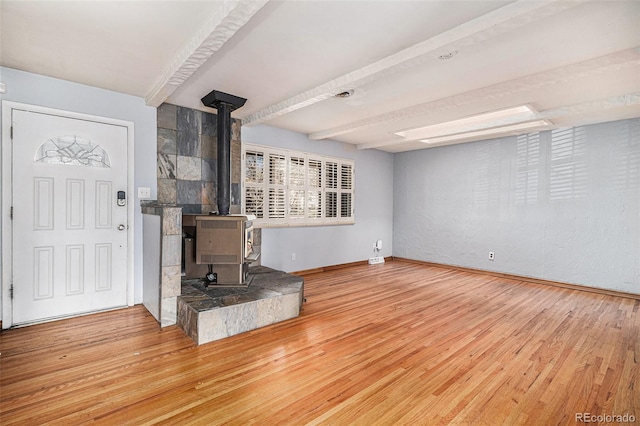 unfurnished living room featuring beamed ceiling, hardwood / wood-style flooring, and a wood stove