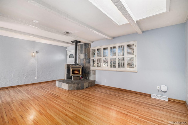 unfurnished living room featuring beamed ceiling, hardwood / wood-style flooring, and a wood stove