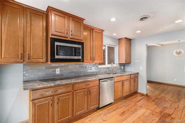 kitchen featuring appliances with stainless steel finishes, tasteful backsplash, sink, dark stone countertops, and light wood-type flooring