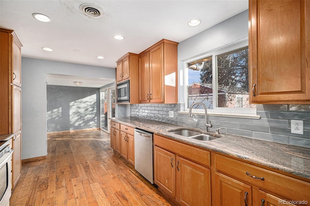 kitchen with appliances with stainless steel finishes, sink, backsplash, and light hardwood / wood-style flooring