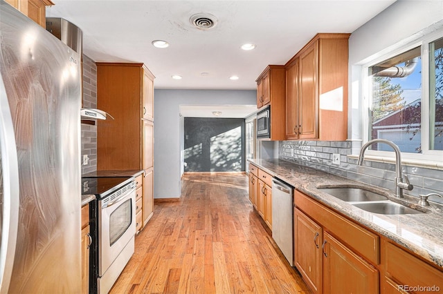 kitchen featuring sink, tasteful backsplash, light stone counters, appliances with stainless steel finishes, and light hardwood / wood-style floors