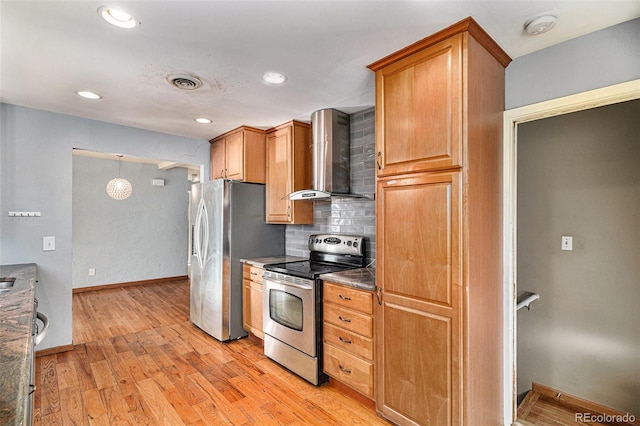 kitchen featuring appliances with stainless steel finishes, backsplash, dark stone counters, light hardwood / wood-style floors, and wall chimney range hood