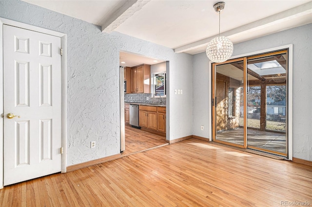 unfurnished dining area featuring beamed ceiling, sink, and light hardwood / wood-style floors