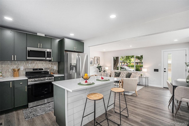 530 Everett St, Lakewood, CO 80226 - kitchen featuring appliances with stainless steel finishes, light countertops, wood finished floors, decorative backsplash, and a kitchen breakfast bar