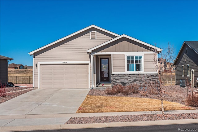 view of front of property featuring an attached garage, central AC, concrete driveway, stone siding, and board and batten siding