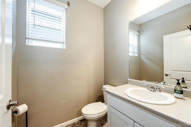 bathroom featuring toilet, a textured wall, baseboards, and vanity