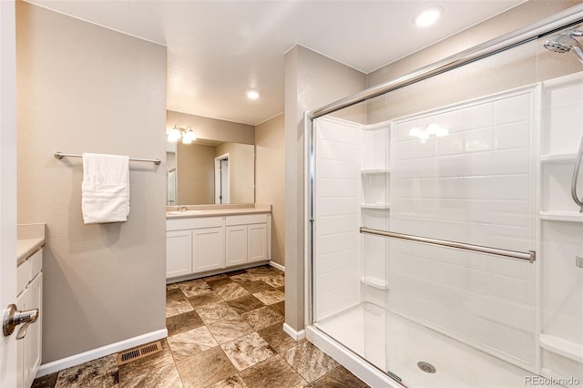 full bathroom with vanity, a stall shower, visible vents, baseboards, and stone finish floor