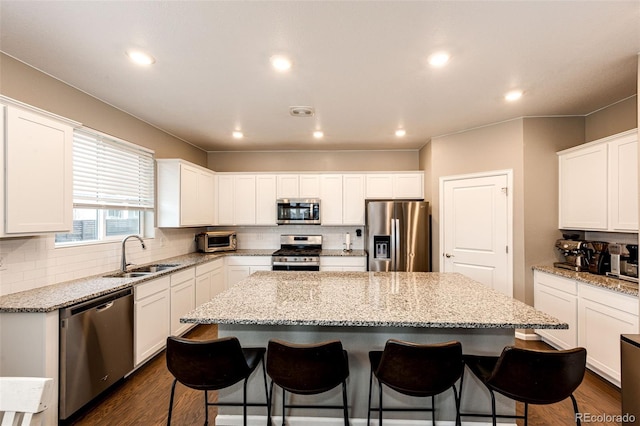 kitchen featuring a breakfast bar, dark wood-style flooring, appliances with stainless steel finishes, a sink, and a kitchen island