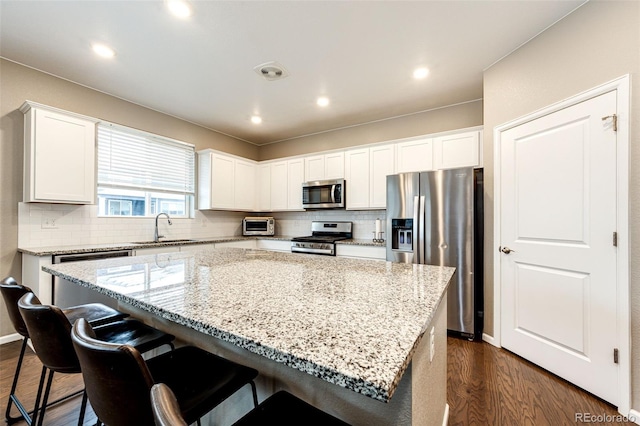 kitchen with dark wood-style flooring, appliances with stainless steel finishes, white cabinetry, a sink, and a kitchen island