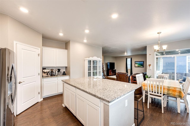 kitchen featuring light stone counters, a center island, dark wood finished floors, white cabinets, and stainless steel fridge