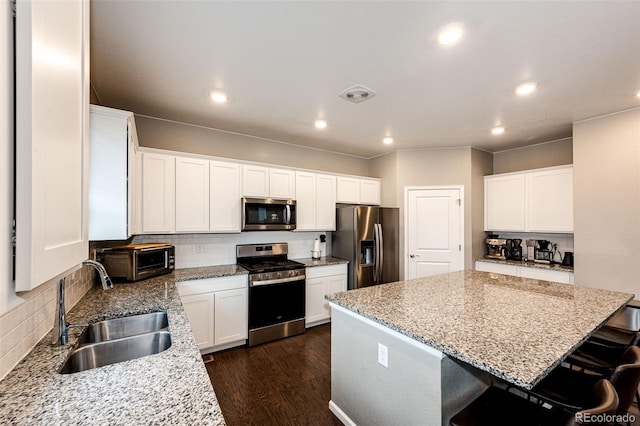 kitchen featuring stainless steel appliances, visible vents, a sink, a kitchen island, and light stone countertops