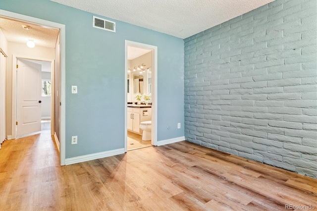 1060 S Parker Rd Unit 25, Denver, CO 80231 - unfurnished bedroom featuring light wood finished floors, a textured ceiling, ensuite bathroom, and brick wall