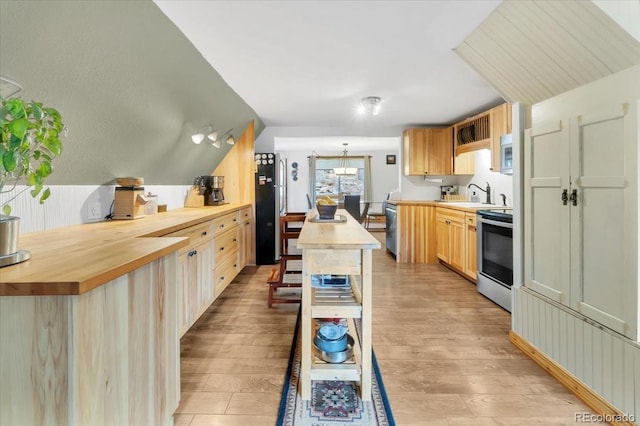 kitchen featuring light wood-style flooring, a center island, wooden counters, light brown cabinetry, and appliances with stainless steel finishes