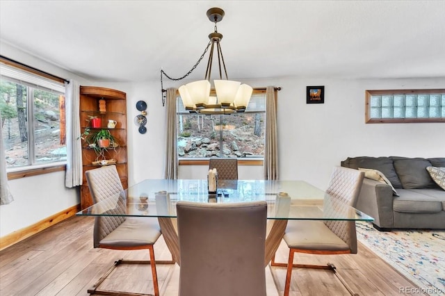 dining room with light wood-type flooring, a wealth of natural light, and a notable chandelier