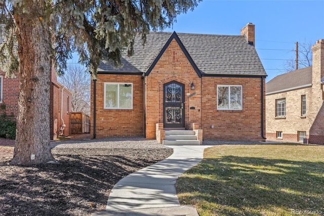 tudor house with brick siding, a front yard, and a shingled roof