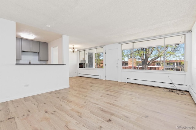 10185 W 25th Ave Unit 33, Lakewood, CO 80215 - unfurnished living room featuring a baseboard heating unit, wood finished floors, a chandelier, baseboards, and a textured ceiling