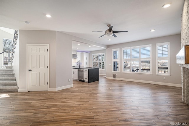 unfurnished living room with stairway, dark wood-style floors, plenty of natural light, a sink, and ceiling fan