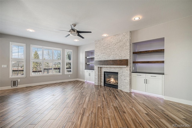 unfurnished living room with a stone fireplace, a healthy amount of sunlight, a ceiling fan, and wood finished floors