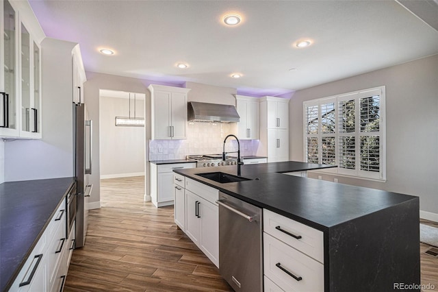 kitchen with a sink, dark countertops, backsplash, stainless steel appliances, and wall chimney range hood