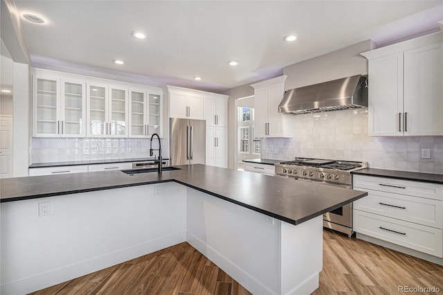 kitchen featuring dark countertops, wall chimney range hood, high quality appliances, and a sink