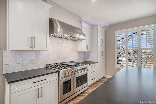 kitchen with tasteful backsplash, double oven range, white cabinetry, wall chimney exhaust hood, and light wood-type flooring