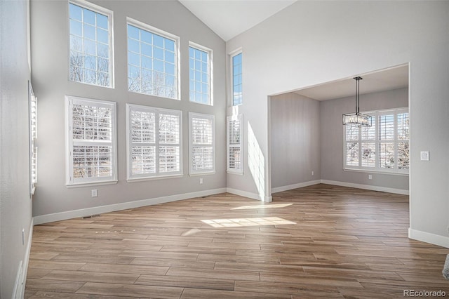 unfurnished room with a chandelier, high vaulted ceiling, baseboards, and wood finished floors