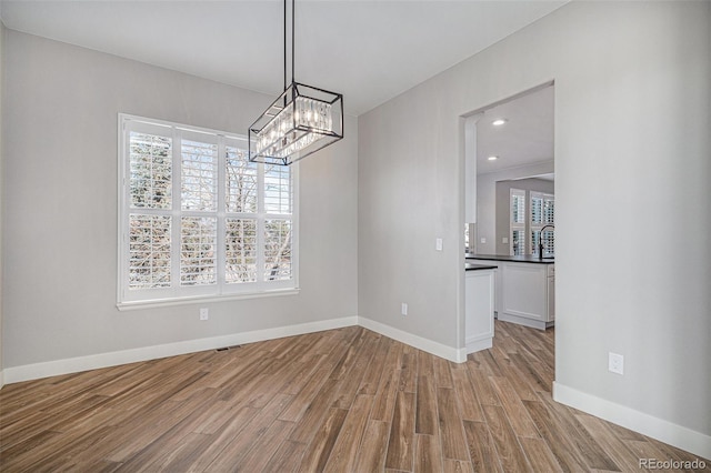 unfurnished dining area featuring recessed lighting, a notable chandelier, light wood-style flooring, and baseboards