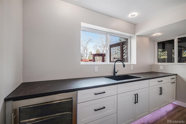 kitchen featuring dark countertops, wine cooler, dark wood finished floors, white cabinets, and a sink