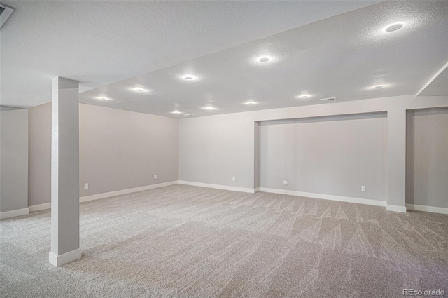 finished basement with light carpet, visible vents, a textured ceiling, and baseboards