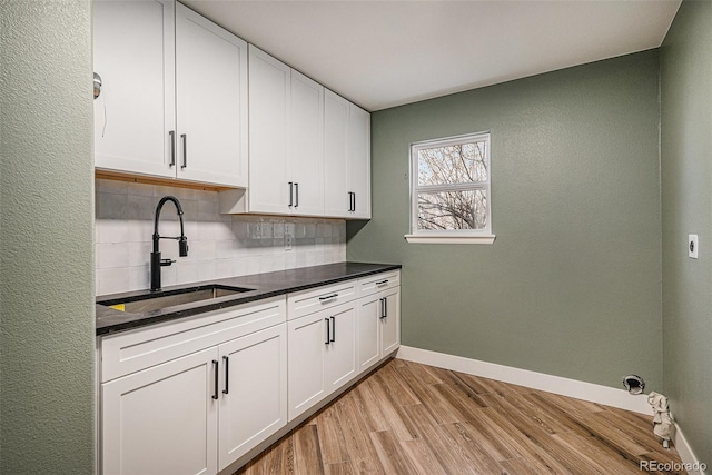 kitchen featuring light wood-style flooring, a sink, backsplash, dark countertops, and white cabinetry