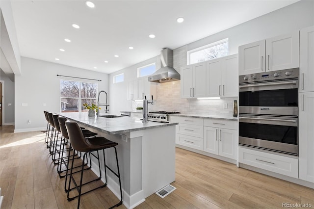 2111 S Franklin St, Denver, CO 80210 - kitchen with double oven, wall chimney exhaust hood, a center island with sink, light stone countertops, and tasteful backsplash